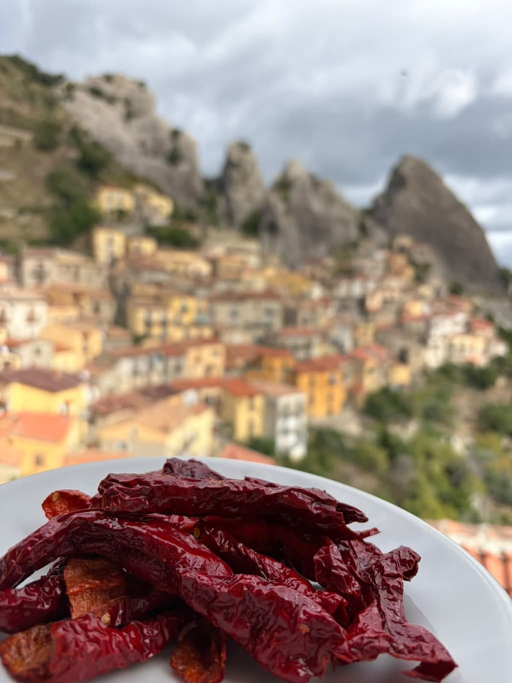 Peperoni cruschi in un piatto, con il paese di Castelmezzano e le guglie sullo sfondo.