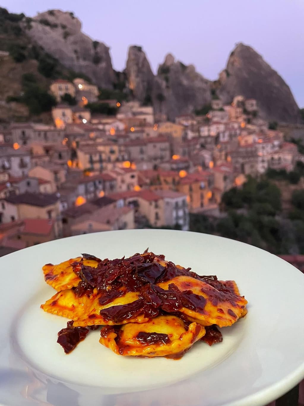 Ravioli ripieni di ricotta conditi con peperoni cruschi, con il paese di Castelmezzano sullo sfondo.
