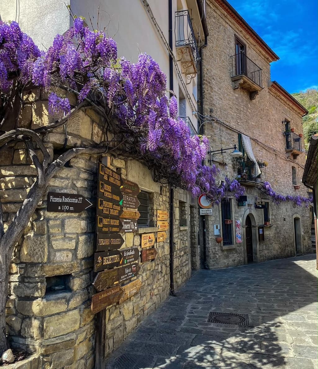 Un vicolo in pietra del centro storico, con il glicine in fiore sul muro e i cartelli in legno dei sentieri.